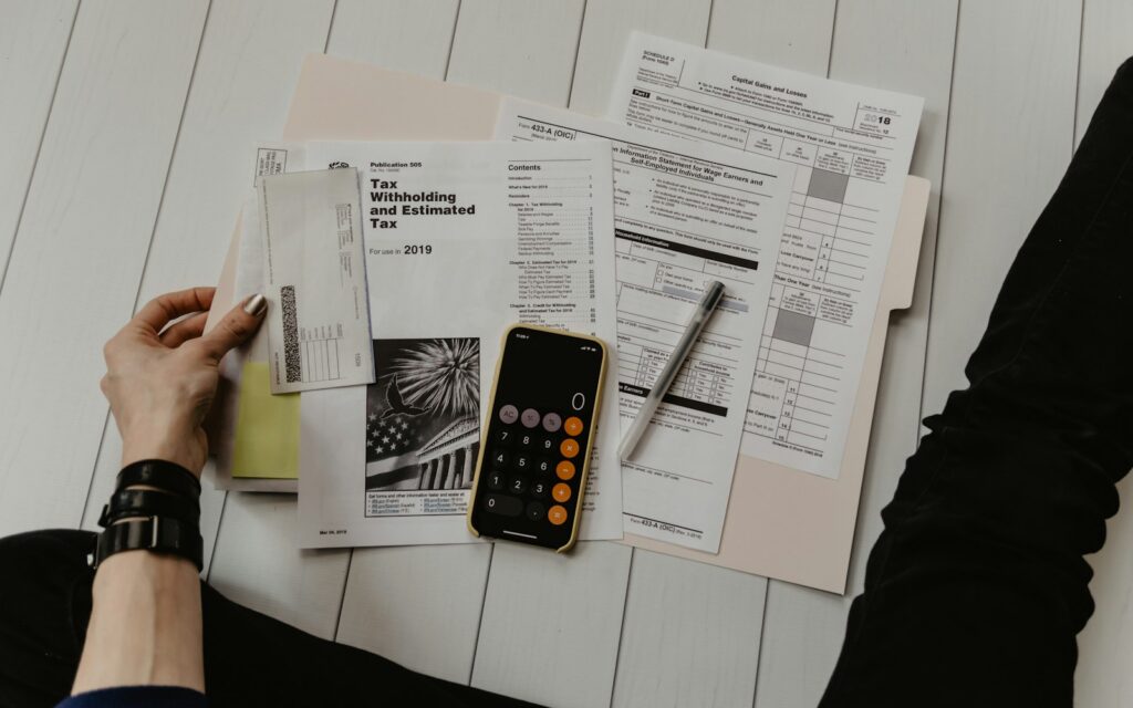 Unterlagen, Taschenrechner und Smartphone auf einem Schreibtisch – Bürokratieabbau im Betrieb