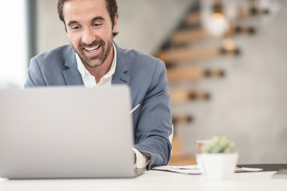 Lächelnder Mann im Videocall am Laptop zum Thema hybride Teams