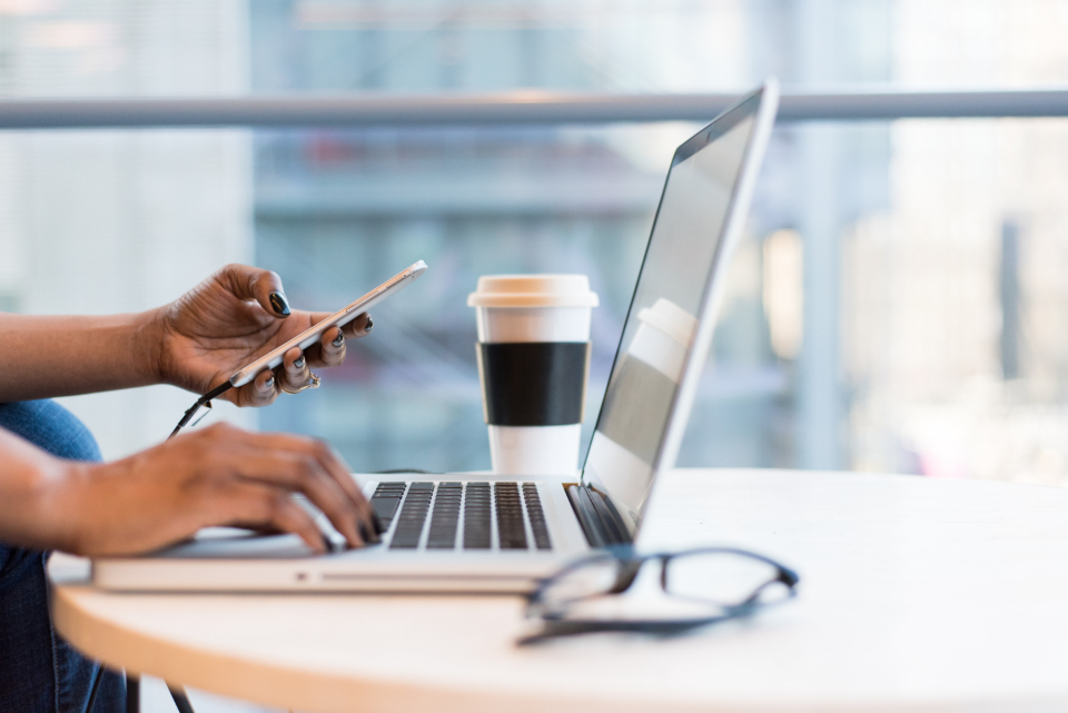 Person mit Smartphone und Laptop am Arbeitstisch zum Thema Newsletter-Marketing