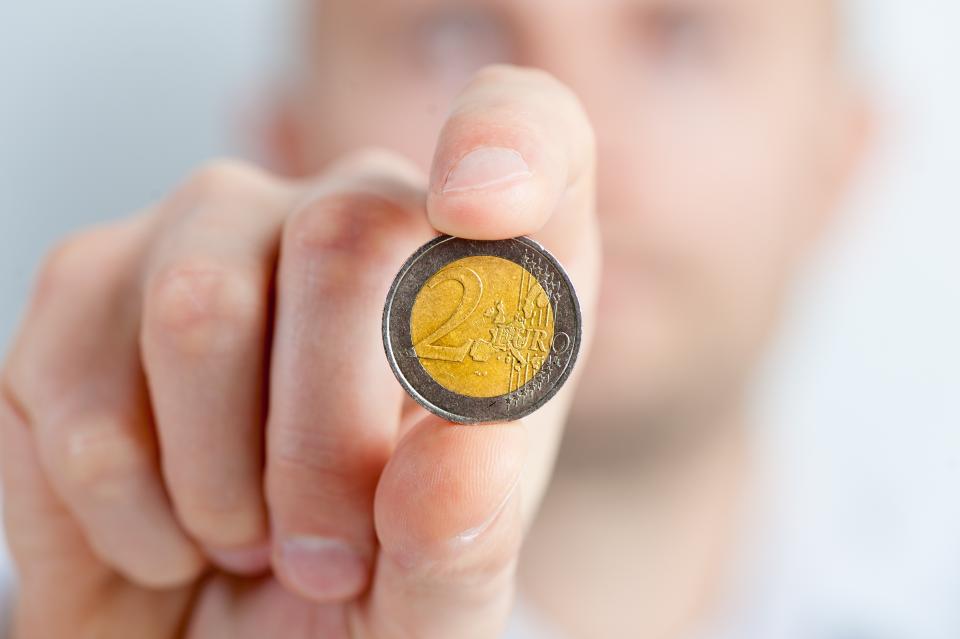 Hand hält eine Zwei-Euro-Münze vor die Kamera