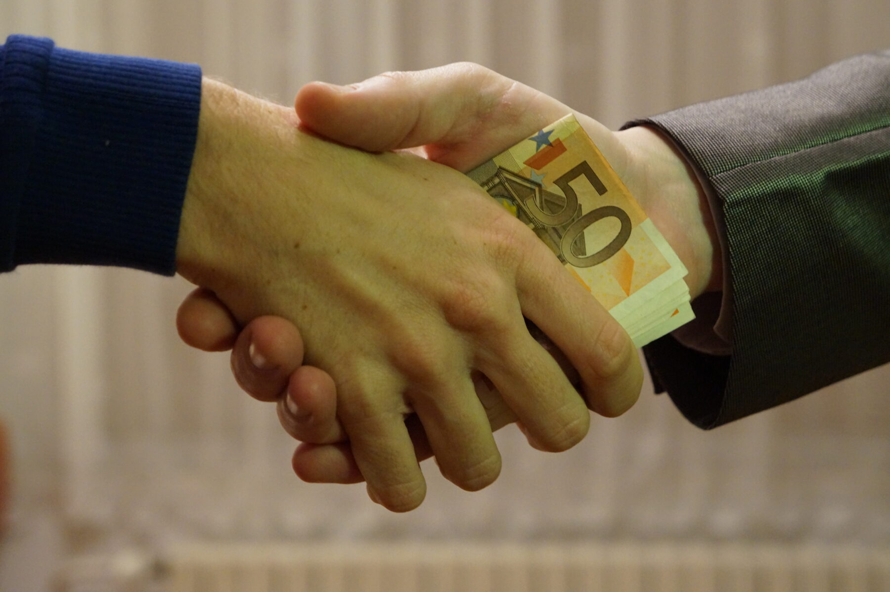Handschlag mit Euro-Banknoten zwischen zwei Geschäftspartnern