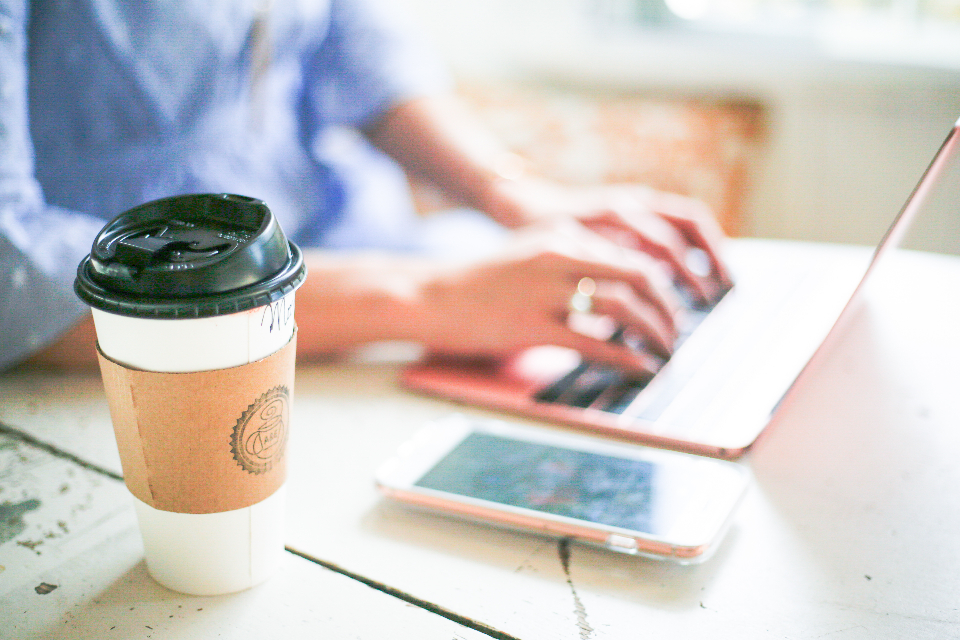 Hände tippen auf einem Laptop neben Kaffeebecher und Smartphone zum Thema Öffnungsrate