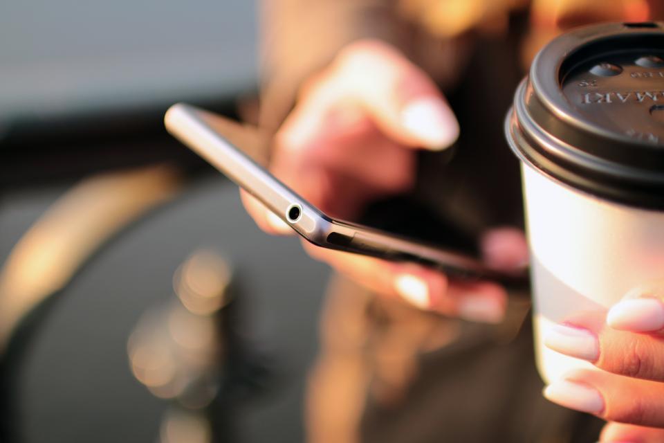 Person liest Nachrichten auf dem Smartphone und hält einen Kaffeebecher