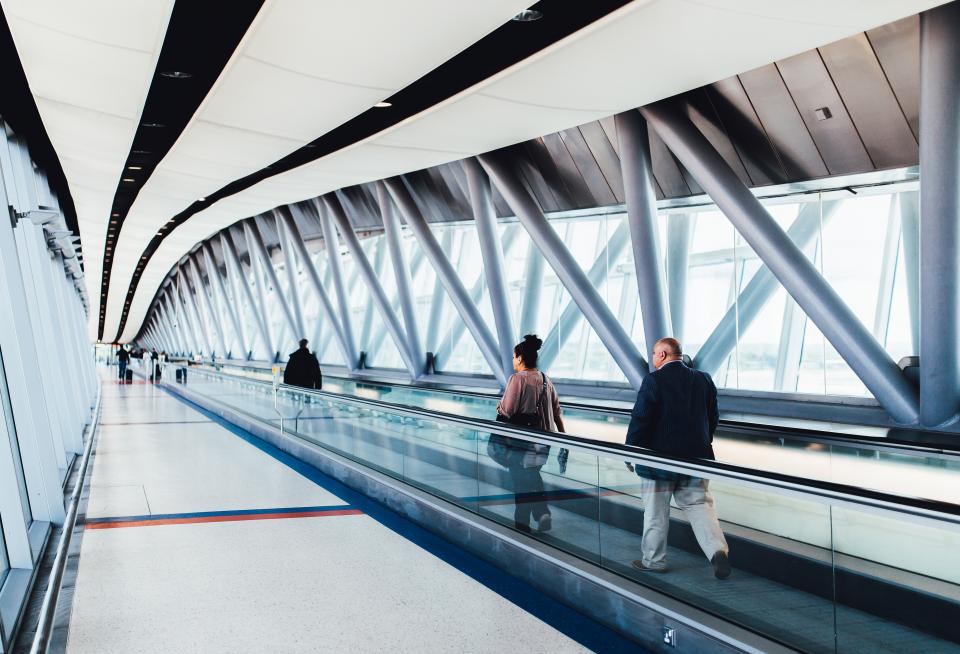 Reisende auf einem Laufband im Flughafen zum Thema Fachkräfteeinwanderung