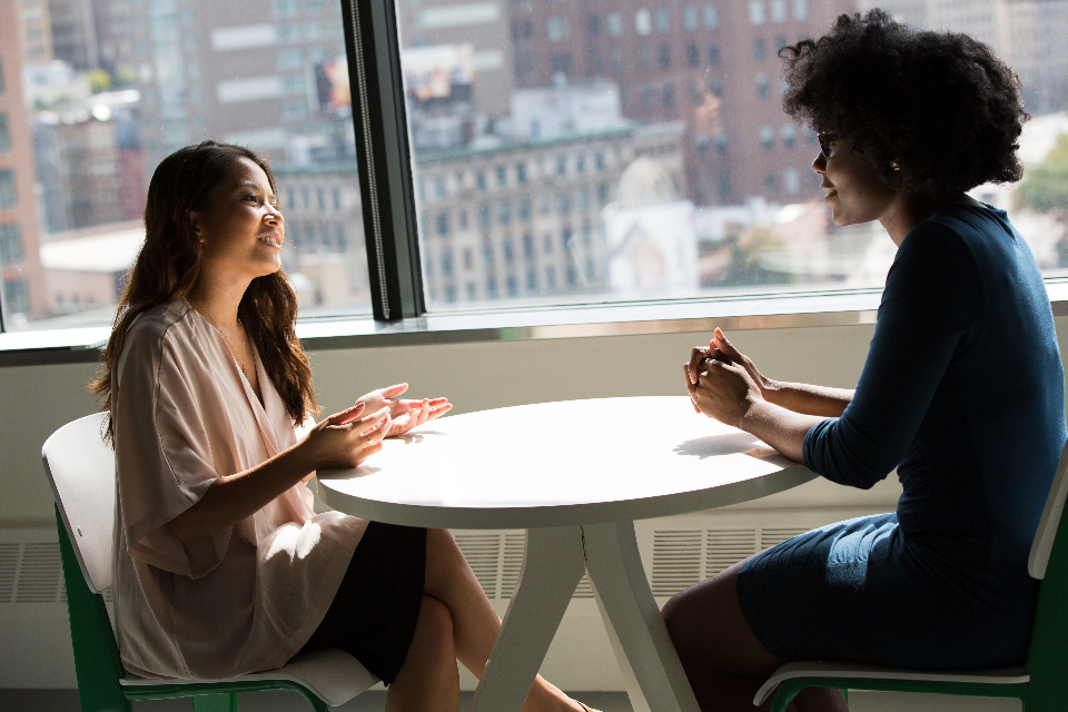 Zwei Frauen im Gespräch an einem runden Besprechungstisch zum Thema Gehaltsverhandlung