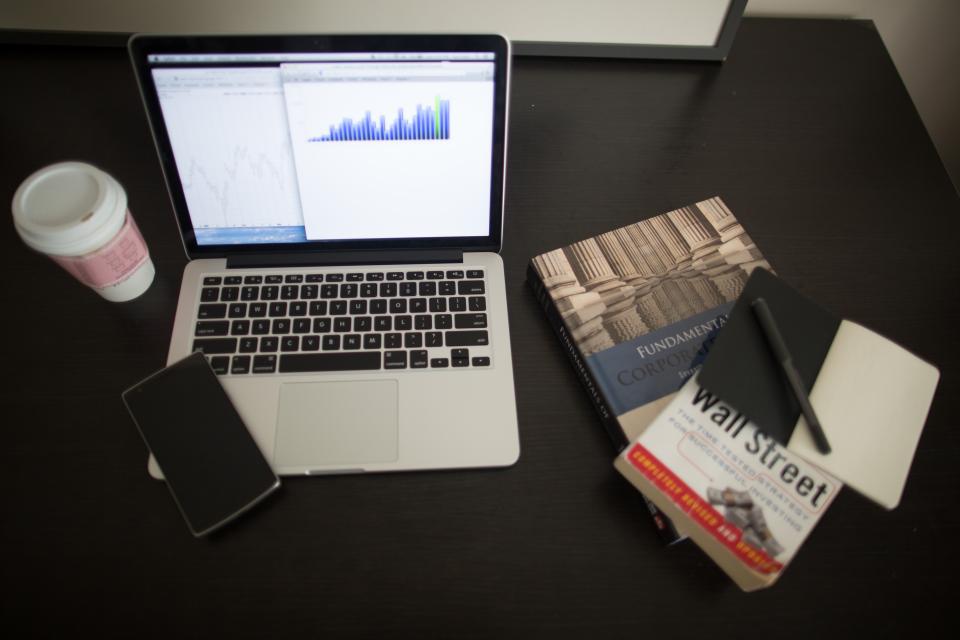 Laptop mit Finanzdiagramm, Smartphone und Wirtschaftsbuch