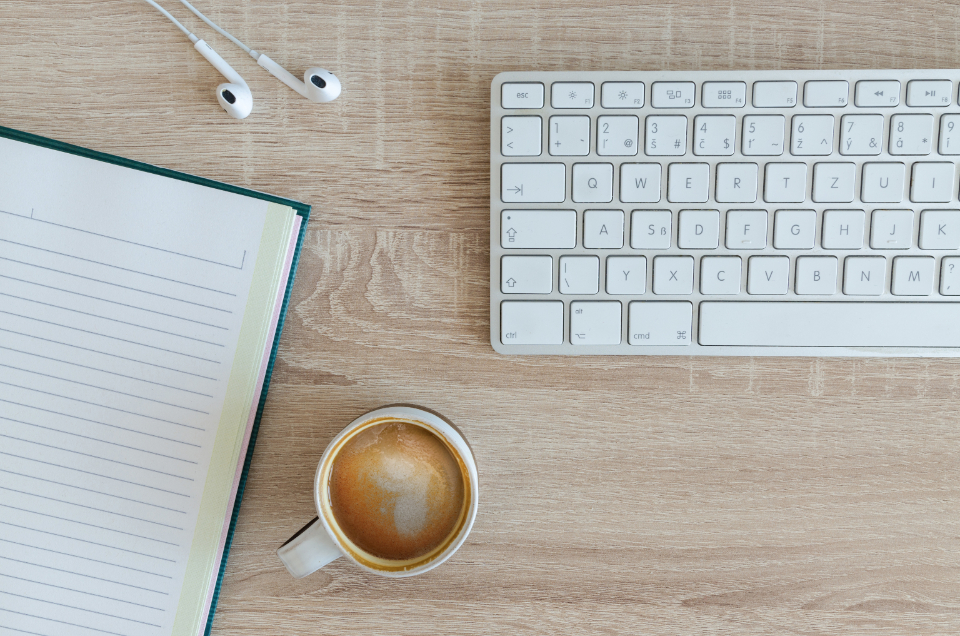 Notizbuch, Tastatur und Kaffee auf einem Schreibtisch